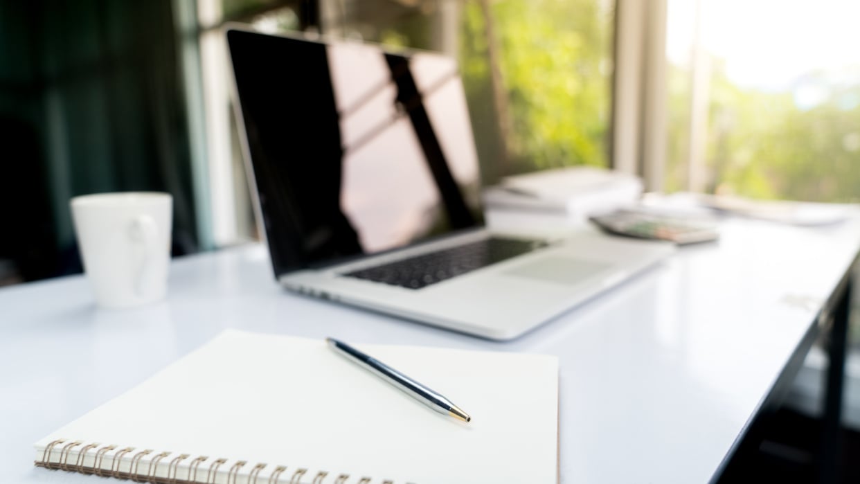 Ein Laptop, Block und Stift liegen auf einem Tisch